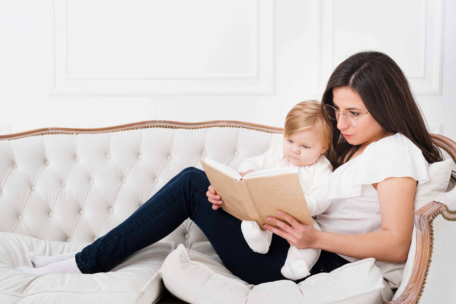 A mother reading a book to her baby on a sofa